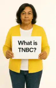 A What is TNBC? sign being held by a latino woman aged 55.